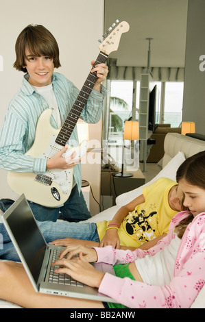 Boy playing a guitar and girl working on a laptop Stock Photo