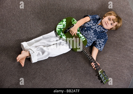 Boy lying on a round sofa and playing a guitar Stock Photo