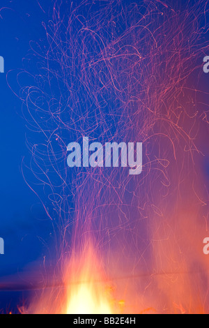 RED AND ORANGE LIGHT TRAILS FROM BONFIRE AGAINST BLUE SKY Stock Photo