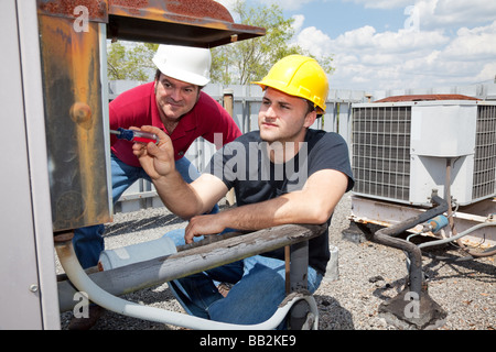 Air conditioning repair apprentice fixes an industrial compressor unit as his supervisor watches  Stock Photo