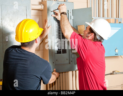 Electricians working together to repair an industrial circuit breaker panel  Stock Photo