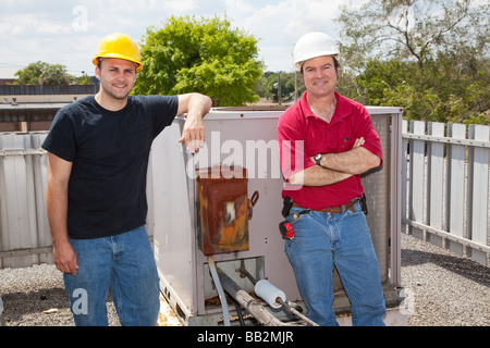 Two air conditioning repair techs standing on a roof in front of an industrial compressor unit  Stock Photo