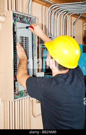 Electrician working on a breaker panel in a control room filled with exposed pipe  Stock Photo