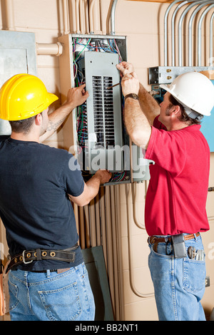 Two electricians repairing an electrical circuit breaker panel in an industrial setting  Stock Photo