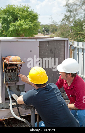 Two AC technicians on a roof repairing an industrial compressor unit  Stock Photo