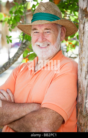 Portrait of a handsome senior man in a Panama hat leaning against a tree  Stock Photo