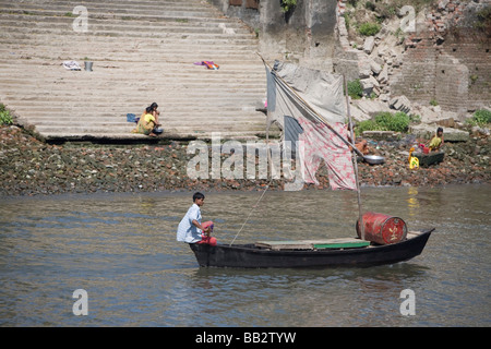 Daily Life in Bangladesh; A boat with a sail made of clothes and cargo aboard passes people on the banks. Stock Photo