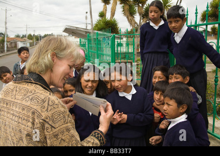 South America, Ecuador, Lasso, female tourist shows postcards to girls and boys  in school uniforms Stock Photo