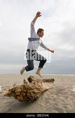 Businessman jumping over a tree trunk on a beach Stock Photo