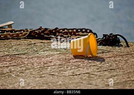 childs seaside bucket left near waters edge on pier next to rusty chains Stock Photo
