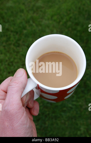 male hand holds spotted mug or cup of tea in left hand with grass below and behind which gives lots of space for copy Stock Photo