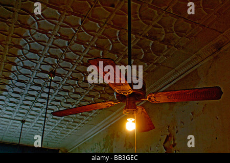 Light burning on an antique ceiling fan under 1920s era ceiling tiles represent out dated energy consumption of yesteryear Stock Photo