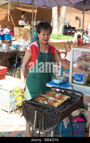 A kebab seller stands by her mobile kitchen grill in a Chiang Mai market Stock Photo