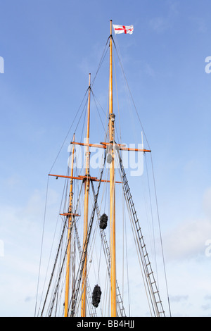 Three wooden masts on restored historic trading schooner with rigging and flying flag of St.George. Stock Photo