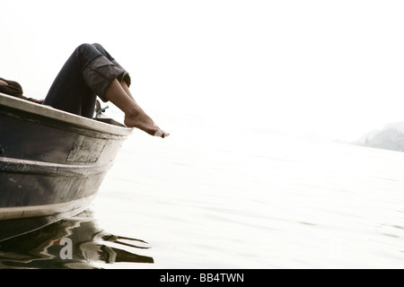 woman feet dangling from rowboat to lake Stock Photo