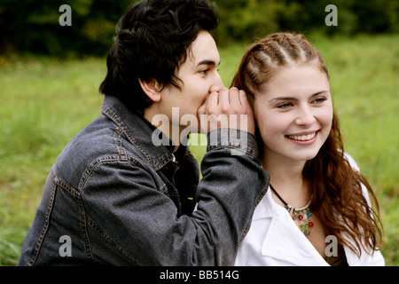 Teenager male whispering into a teenager female ear Stock Photo