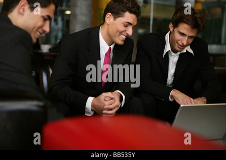 three men are looking on a laptop in a lounge Stock Photo