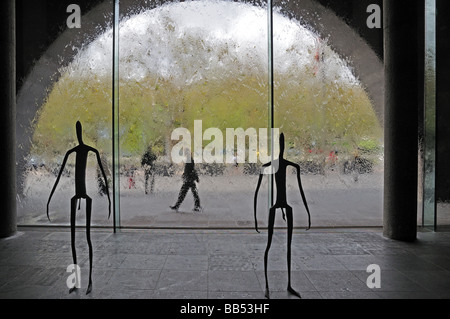Metal sculpture human stick figures inside Victoria National Gallery Melbourne Australia with glass wall a running water