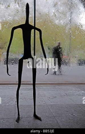 Metal sculpture human stick figure inside Victoria National Gallery Melbourne Australia with glass wall of running water