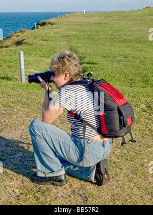 Lady crouching to take photograph with a DSLR camera supporting camera with elbow on knee Stock Photo