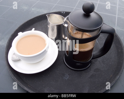 A cup of coffee a cafetiere and a milk jug on a table outside a café Stock Photo