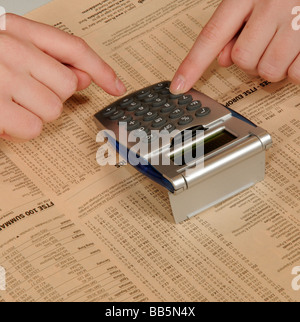 Fingers working on a calculator to check world market prices from a financial newspaper page Stock Photo