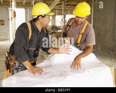 Hispanic workers looking at blueprints on construction site Stock Photo