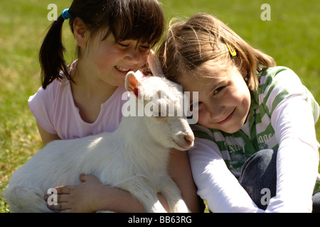 Girls hugging goats in grass Stock Photo