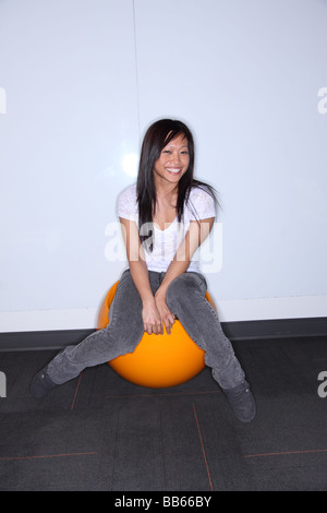 Asian woman sitting on orange ball smiles Stock Photo