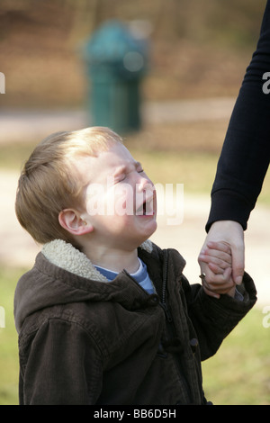 Two year old boy hold a parents hand crying with his eyes shut. Stock Photo