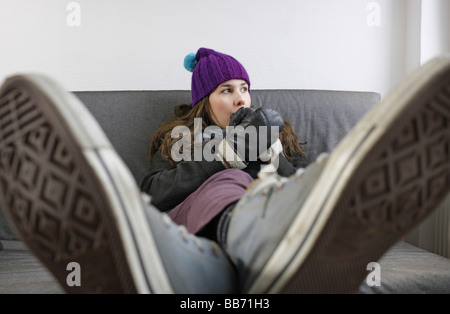Saving heating coasts young woman at home wearing a cap and gloves Stock Photo