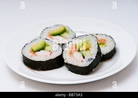 A white plate with four sushi maki rolls containing rice, salmon, avocado and cucumber wrapped in nori, seaweed. Stock Photo