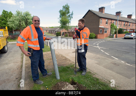 Two utility workers in high visibility jackets installing or repairing roadside infrastructure on a quiet residential street in a suburban neighborhoo Stock Photo