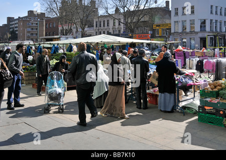 Shoppers on pavement around stalls in busy crowded Whitechapel outdoor street market in East London Borough of Tower Hamlets England UK Stock Photo