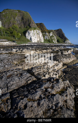 The A2 causeway coastal route coast road at Garron Point under Limestone and basalt cliffs with basalt rock formations Stock Photo