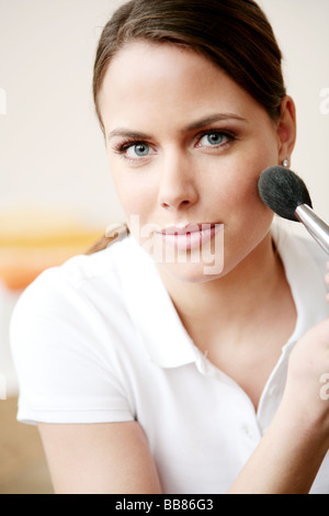 Portait of young beauty woman applying powder with a brush on cheek Stock Photo