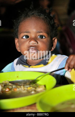 Small, dark skinned, cross-eyed girl in a soup kitchen, slums of Alto de Cazuca, Soacha, Bogotá, Columbia Stock Photo