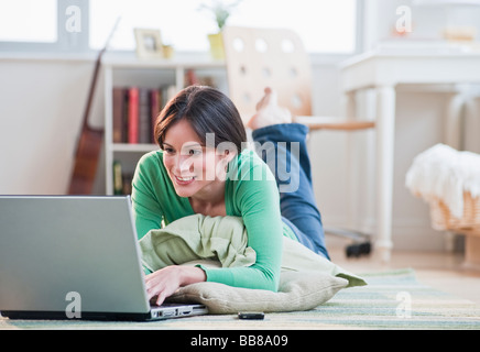 Mid-adult woman lying on floor using laptop Stock Photo