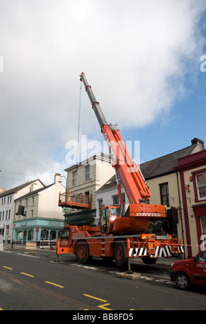 Large orange crane on carmarthen town centre lifting goods out of first floor property plant hire Stock Photo