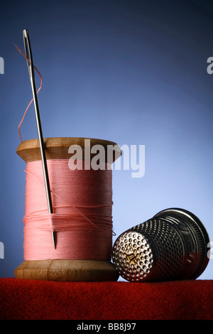 a wood spool of pink thread with the needle stuck in it and a thimble Stock Photo
