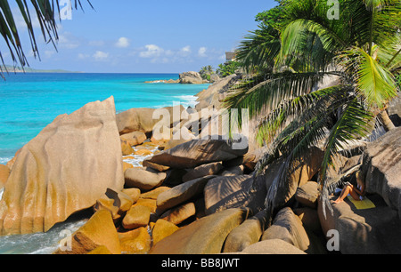 Woman sitting on a rock in the shade of palm trees, Anse Patates, La Digue, Seychelles Stock Photo