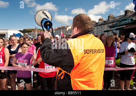 Male supervisor wearing orange tabard holding a megaphone giving instructions to women competing in the Race For Life 2009 Stock Photo