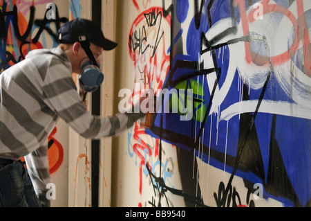 Teenage boy working on a grafitti piece on an interior wall while wearing a respirator. Stock Photo