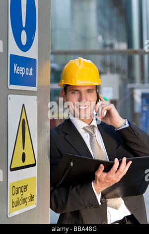 A male manager on a construction site wearing a hard hat and talking on his phone Stock Photo