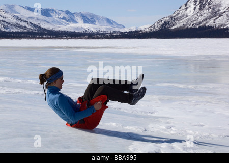 Woman playing, sliding down ice hill on her bottom, overflow, glaciation, ice building up on the shore of Fish Lake, spring, Yu Stock Photo