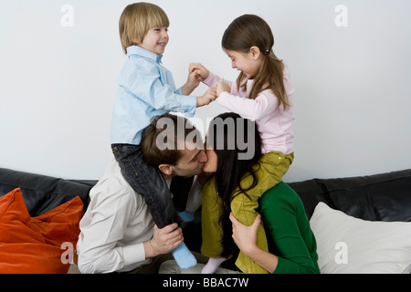 Two parents carrying children on their shoulders and kissing Stock Photo