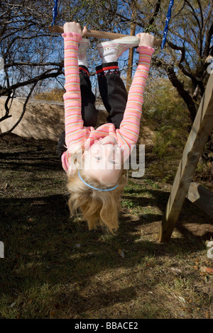 A young girl hanging upside down from a swing Stock Photo