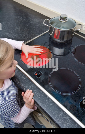 A young girl holding her hand over a hot electric stove burner Stock Photo