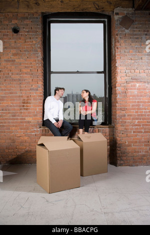 A couple sitting on the window sill with cardboard boxes Stock Photo