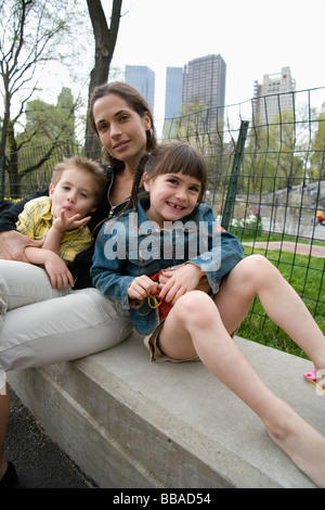 A woman and her children sitting together on a park bench, Central Park, New York City Stock Photo
